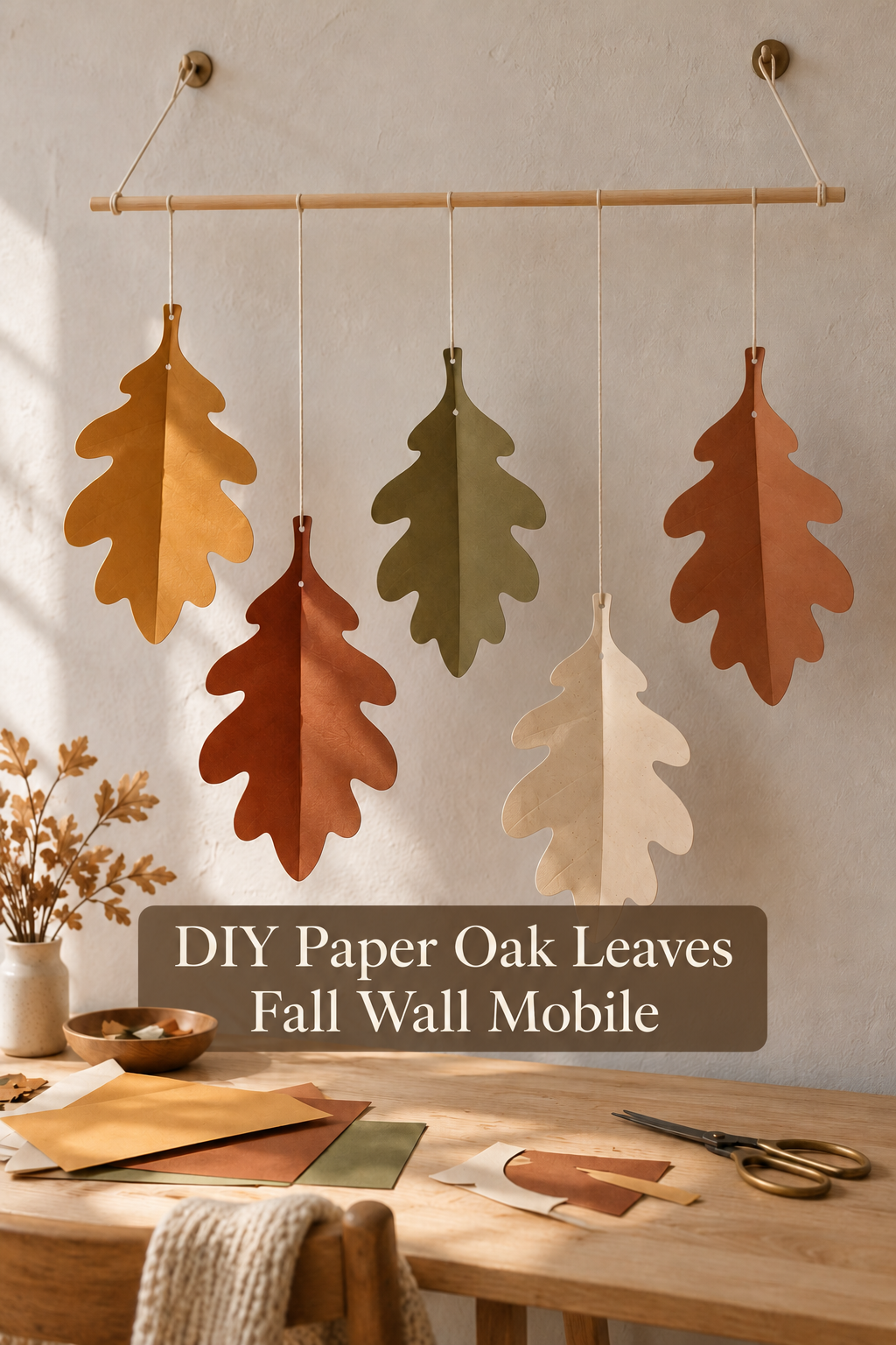 Folded autumn paper oak leaves hanging from a wooden rod above a craft table.