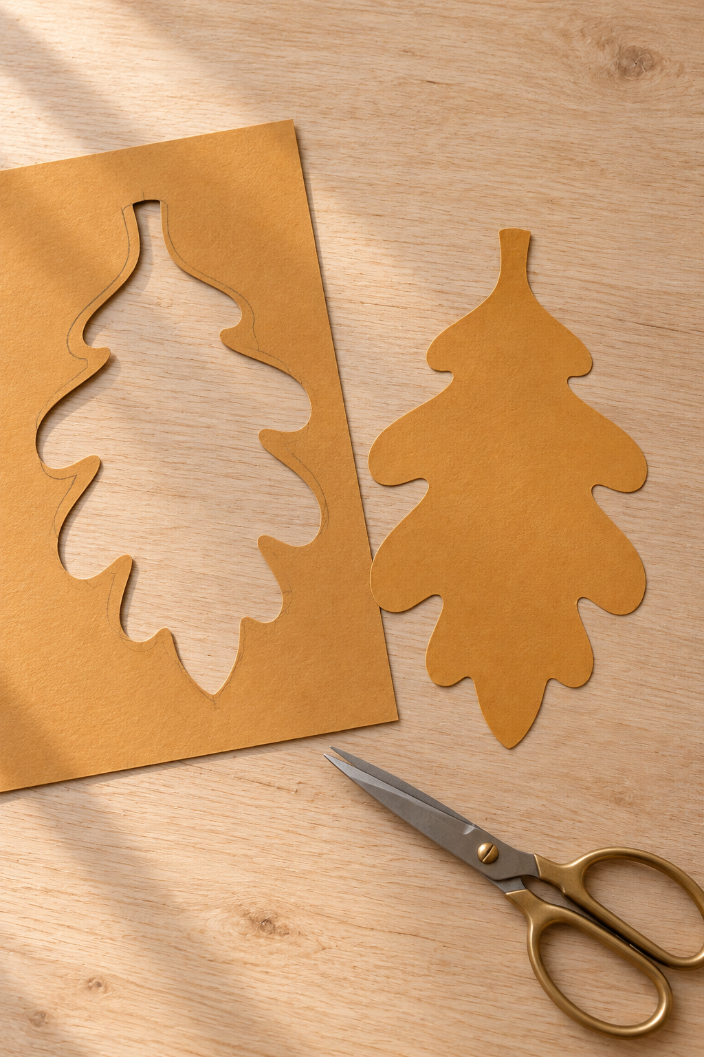 Cut ochre cardstock oak leaf beside its matching offcut and craft scissors.