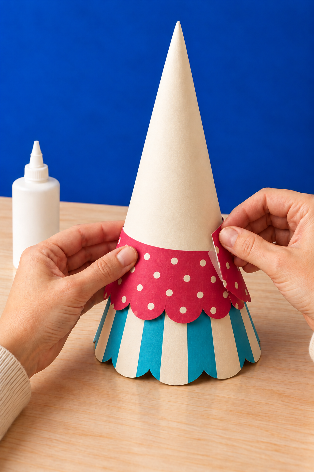 Hands overlap a raspberry paper band above a turquoise striped tier on a cone.