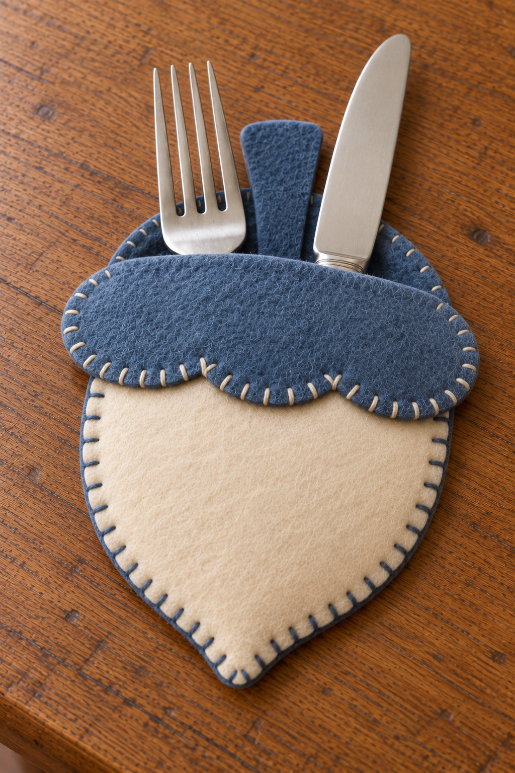 Fork and knife inserted into the open top of a blue and ivory felt acorn pocket.