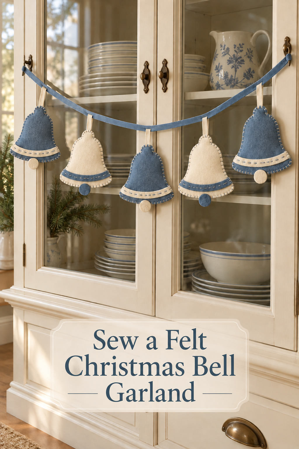 Blue and ivory felt Christmas bells hang from ribbon across a cream glass-front cabinet.