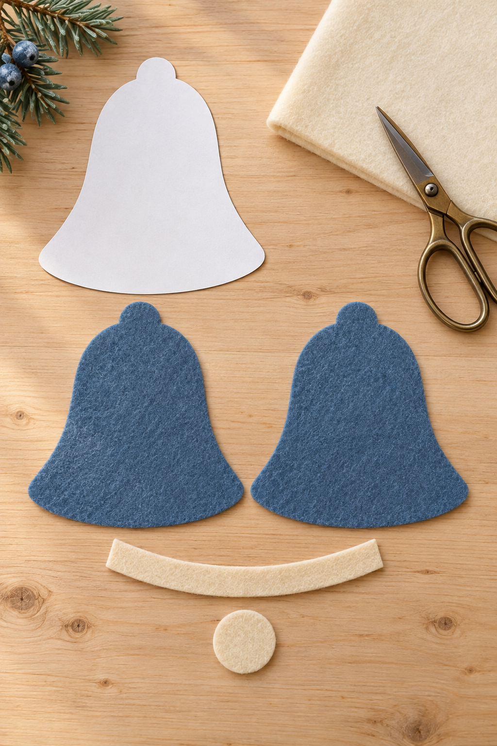 Two blue felt bell cutouts lie beside an ivory band, round clapper, and paper pattern.