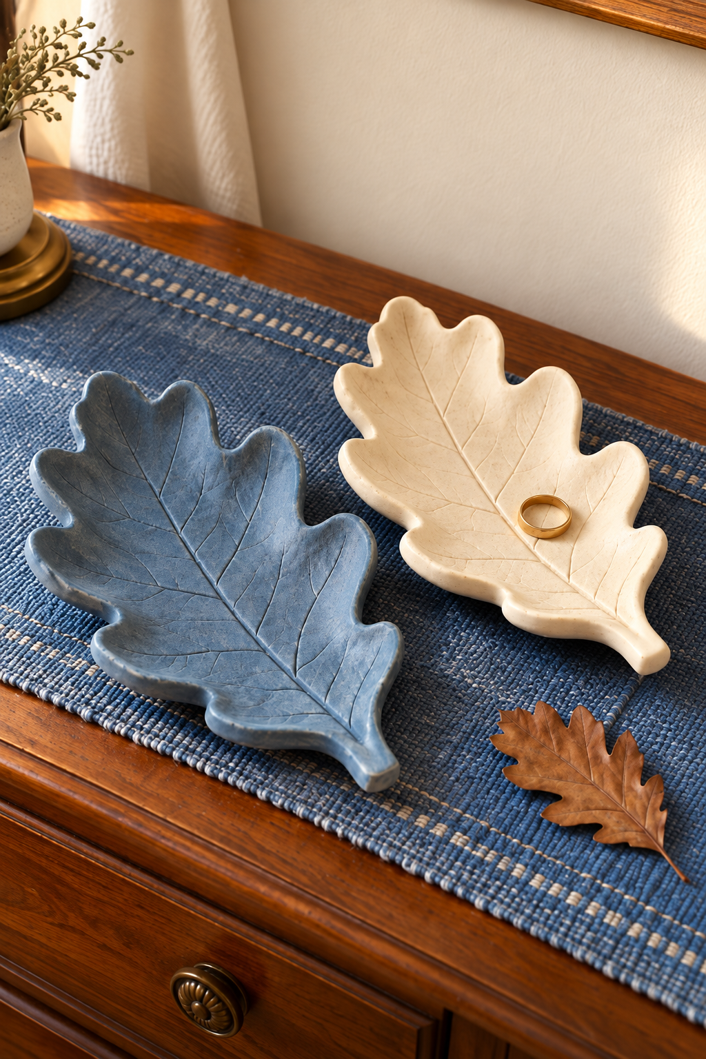 Blue and ivory oak-leaf clay dishes with impressed veins on a woven dresser runner.
