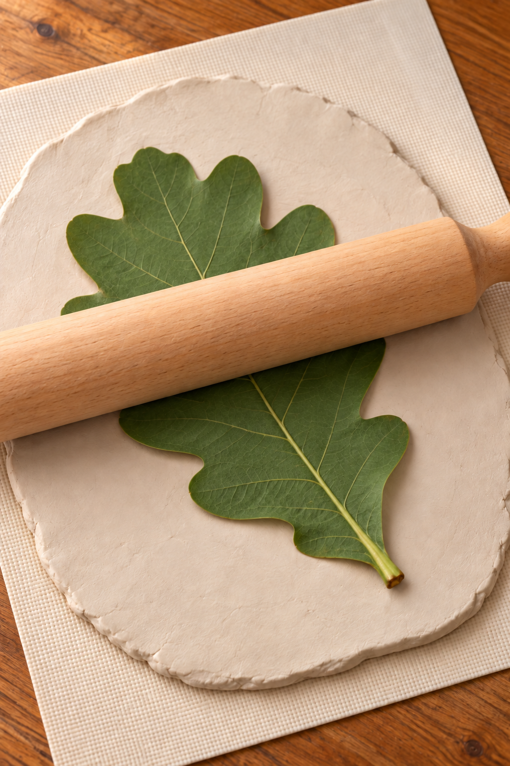 Oak leaf on a pale clay slab with a rolling pin resting across it for vein impressions.