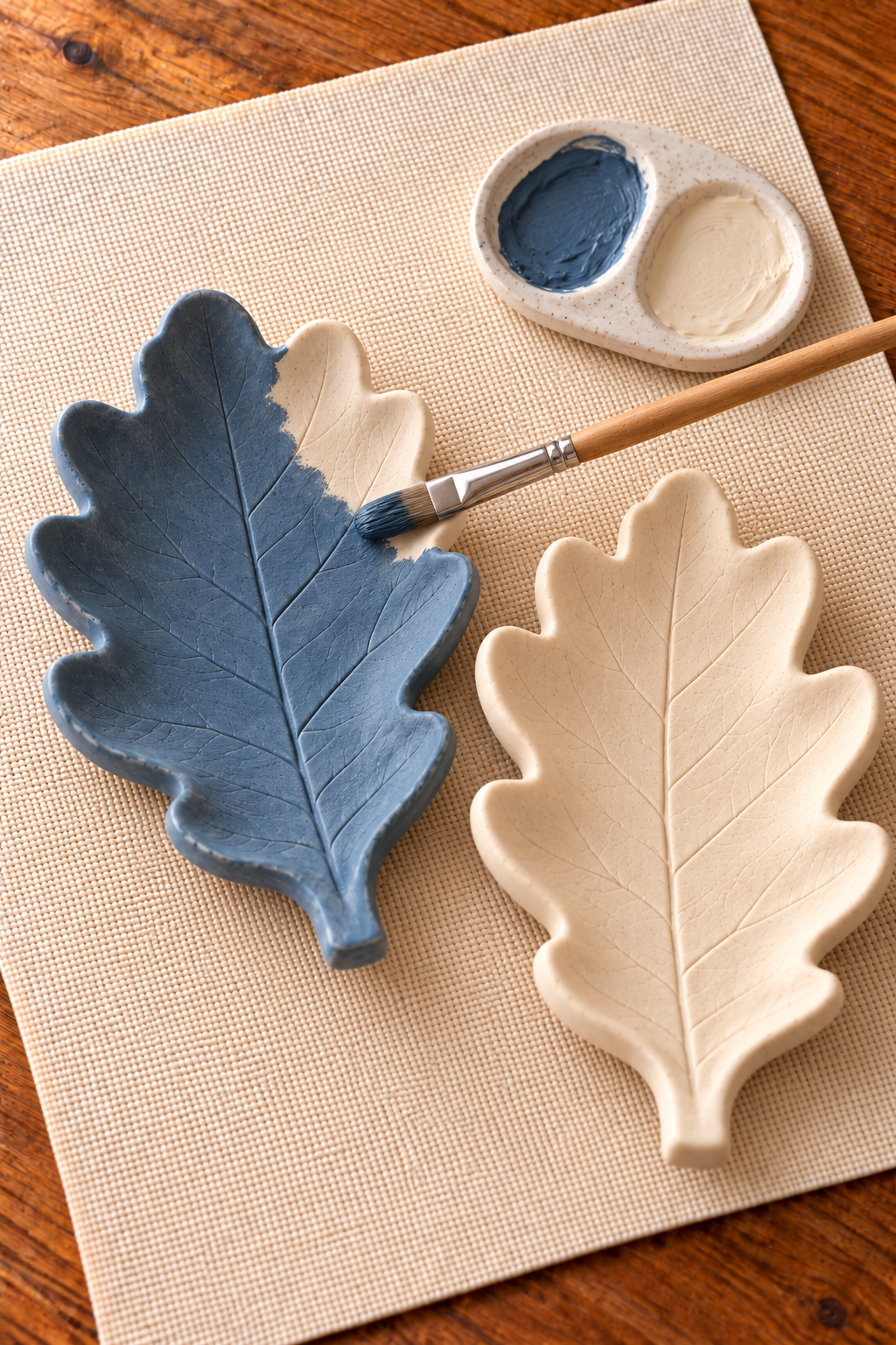 Partly blue-painted leaf dish beside an ivory dish, with a paintbrush and two-color palette.