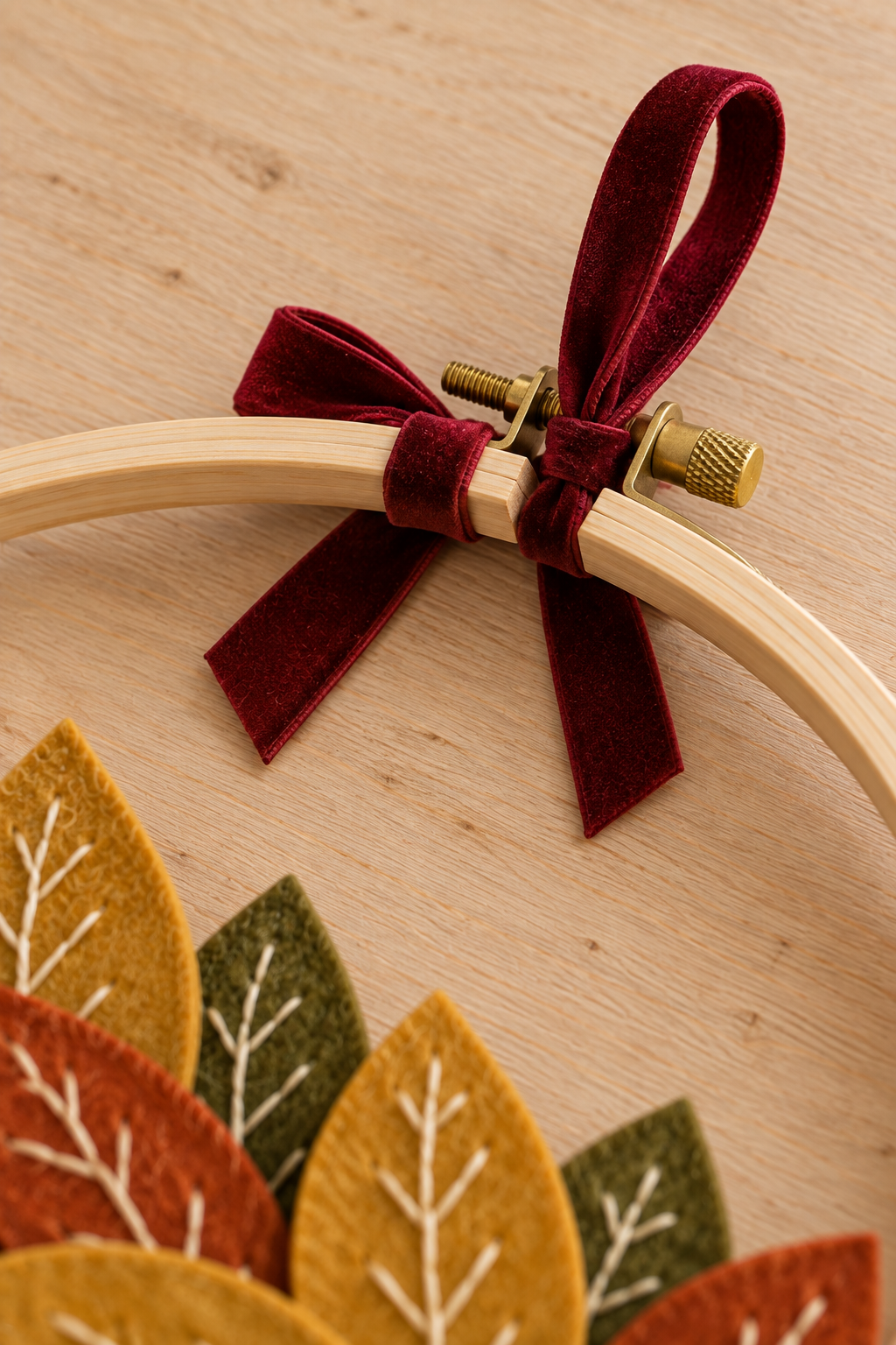 Burgundy velvet loop and bow tied around the top of a wooden hoop beside its brass screw.