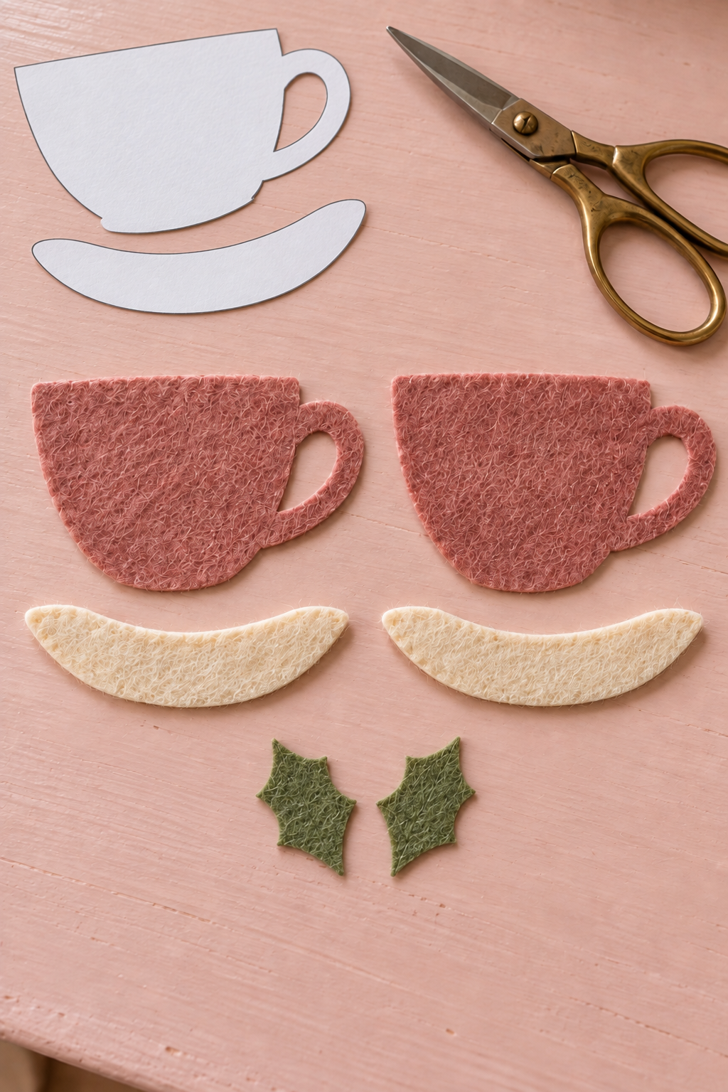 Dusty rose felt cup layers, cream saucers and two holly leaves laid out for sewing.