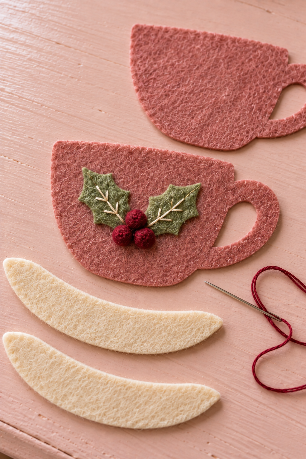 Holly leaves and burgundy felt berries stitched onto a flat rose felt cup front.