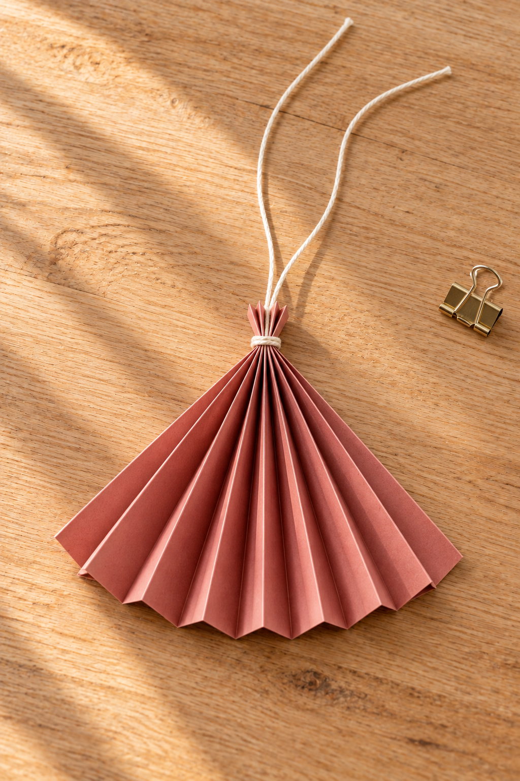 Cream cord tied around the gathered top of a rose paper fan skirt on a work surface.