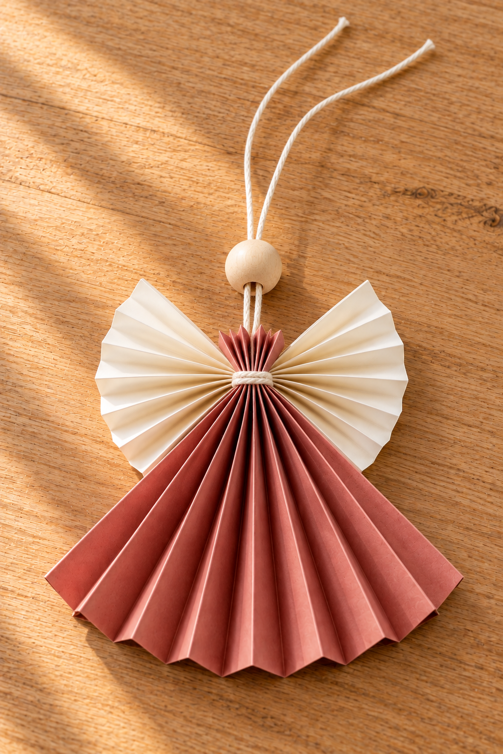 Two cream cords pass through a wooden bead above a rose paper skirt and cream wings.