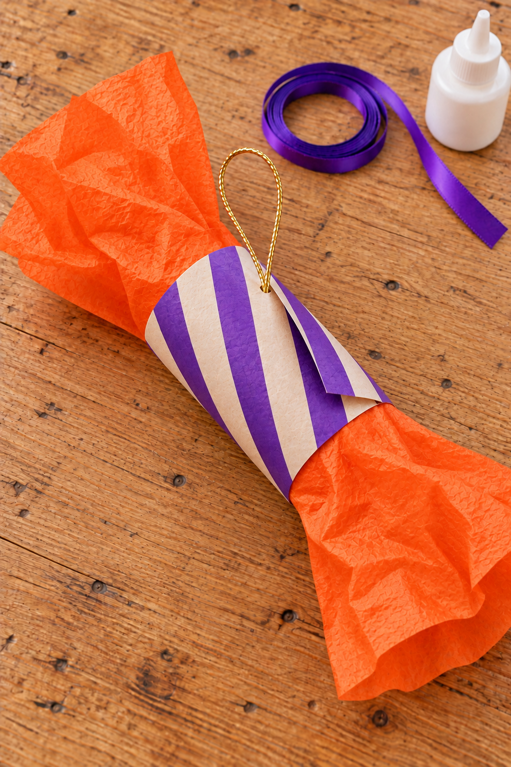 Violet-striped paper sleeve partly wrapped over orange tissue with a gold hanging loop.
