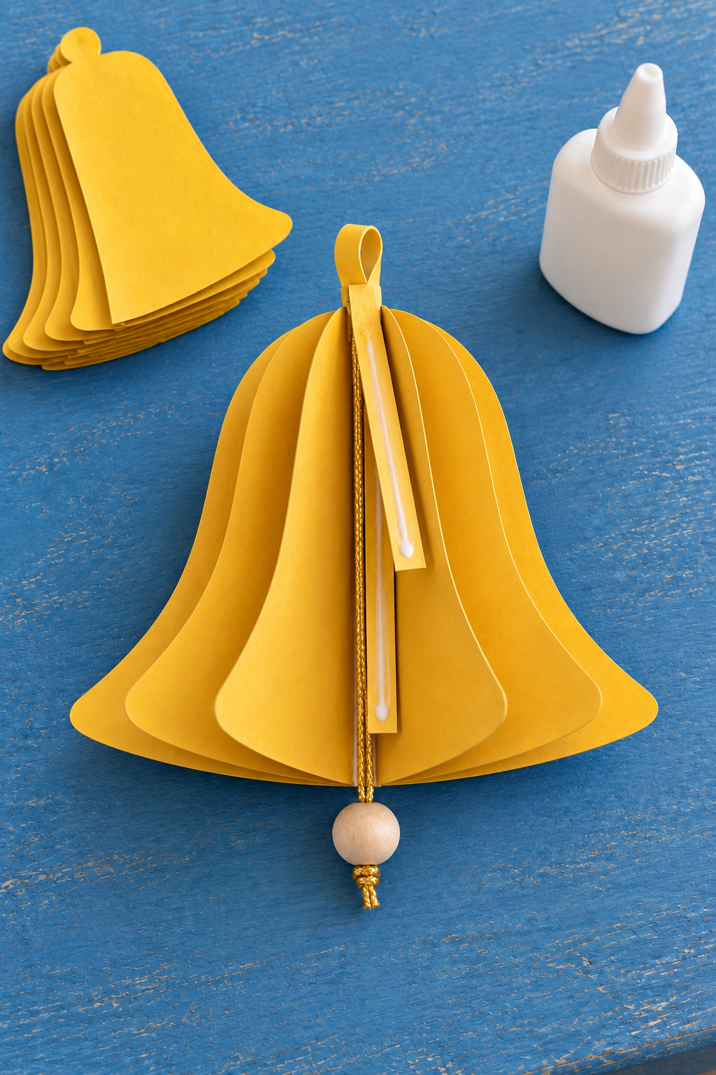 A gold bead cord and paper loop tails lie along an open yellow bell's central spine.